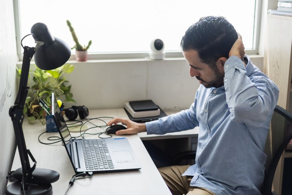 Mann sitzt am Schreibtisch im Homeoffice und hält sich den Nacken