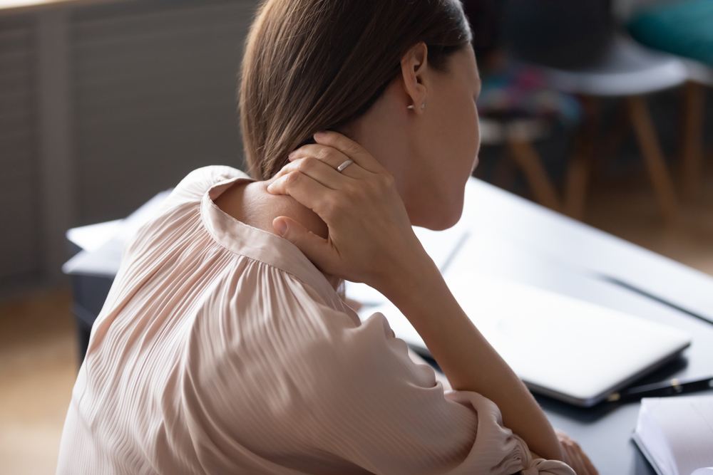 Junge Frau von hinten am Schreibtisch, Hand am Nacken